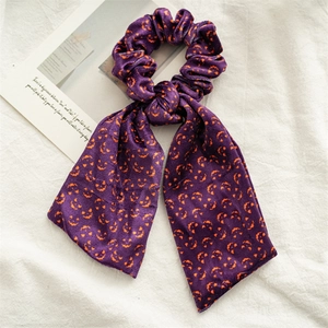 Dettaglio macro dello scrunchie di Halloween in velluto viola con zucche e nastri decorativi