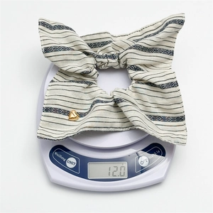 Close-up of a striped bow hair scrunchie weighing 12 grams on a white digital scale
