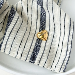 Detailed close-up of a heart-shaped golden brooch with Hammer engraving on striped fabric