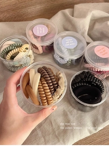 Close-up of Morandi colored hair ties in a transparent jar on a beige linen background
