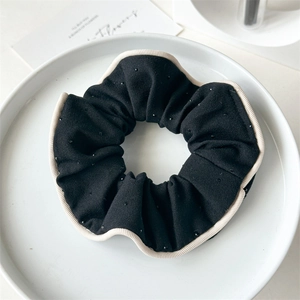 Detail of black fabric hair scrunchie with beige wavy edges and subtle glitter dots