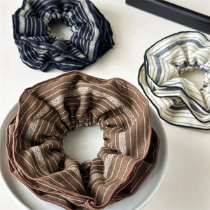 Detailed texture of striped fabric scrunchies in brown, navy, and beige colors