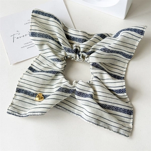 Detail of blue and white striped bow scrunchie with a gold heart charm engraved Lucky