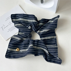Detail of navy striped fabric scrunchie with a gold heart pendant on white background