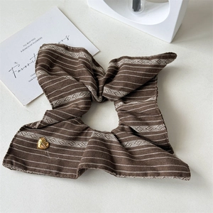 Close-up of brown striped fabric hair tie with a gold heart pendant and textured finish