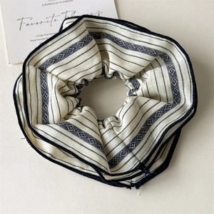 Close-up of beige fabric scrunchie with navy blue stripes and geometric patterns