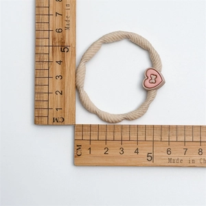 Détail de l'élastique beige torsadé avec breloque cœur rose mesurant 5cm de diamètre