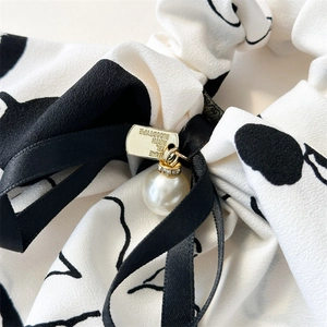 Detail of ink style scrunchie with pearl, ribbon and engraved golden metal tag