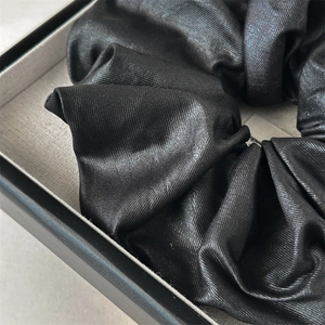 Gros plan détaillé d'un chouchou en satin noir montrant la texture du tissu plissé lisse