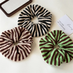 Close-up of three knitted striped hair scrunchies in black, brown, and green colors