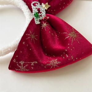 Detail of red velvet Christmas bow headband with gold star patterns and Merry Christmas charm