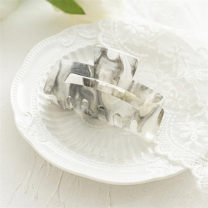 Detail shot of large marble-patterned acrylic hair claw with silver sequins on white lace