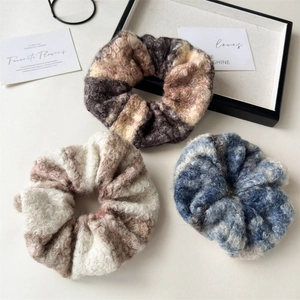 Three oversized plush wool scrunchies in brown, beige, and blue grey on a tray