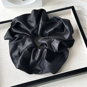 Détail d'un chouchou noir avec texture brillante métallique et design plissé élégant
