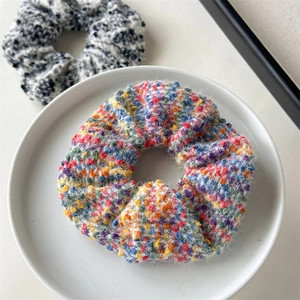 Detailaufnahme des gestrickten Regenbogen-Haargummis auf einem weißen Keramikteller