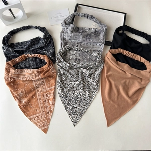Five assorted paisley and leopard print bohemian elastic headbands laid flat on a beige surface