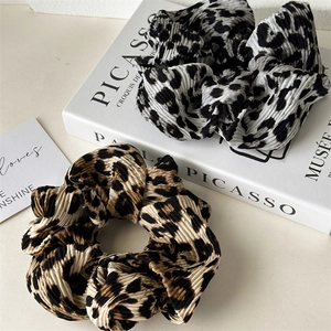 Detail view of two pleated leopard print scrunchies in brown and black on a white table