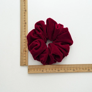 Detail of burgundy velvet scrunchie size measuring 13.5cm on a white scale background