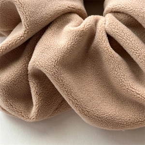 Detailed macro view of soft camel-colored plush velvet scrunchie showing fabric texture