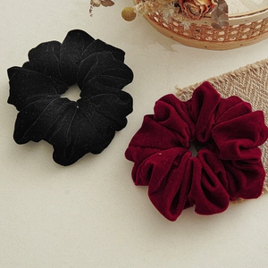 Detailed view of black and burgundy velvet scrunchies on a rustic textured background