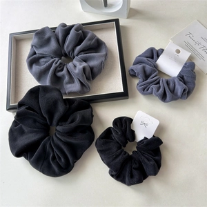 Close-up of plush velvet scrunchies in dark grey, blue and black on a minimalist tray