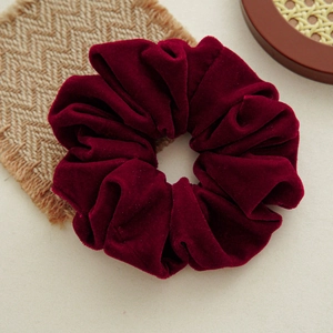 Detail of burgundy velvet scrunchie with glossy texture and elegant pleated style