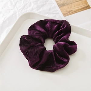 Dettaglio di un elastico in velluto viola scuro con consistenza morbida su vassoio bianco