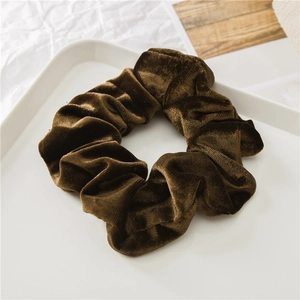 Dettaglio dell'elastico per capelli in velluto marrone scuro su vassoio in ceramica bianca