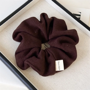 Detailed close-up of dark brown knitted scrunchie with handmade fabric label on tray