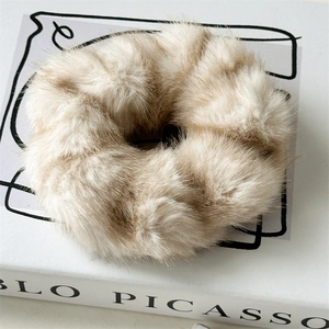 Gros plan sur un chouchou en fausse fourrure beige posé sur un livre d'art minimaliste