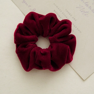Detail of burgundy velvet scrunchie showing soft texture and pleated design on fabric
