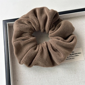 Macro shot of coffee brown plush scrunchie showing soft faux fur texture on a linen tray