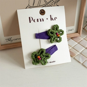 Detail showing two handmade crochet olive flower hair clips with purple fabric wrapped bases