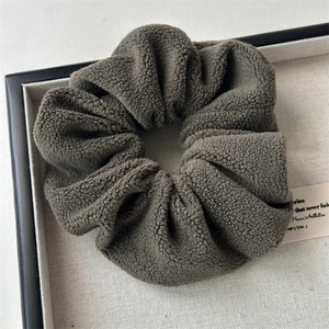 Close-up of dark brown plush velvet hair scrunchie with soft fleece texture in a display tray