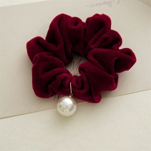 Macro detail of red velvet scrunchie featuring a large white faux pearl gold pendant