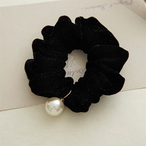 Detail view of a black velvet scrunchie featuring a large pearl charm and subtle glitter
