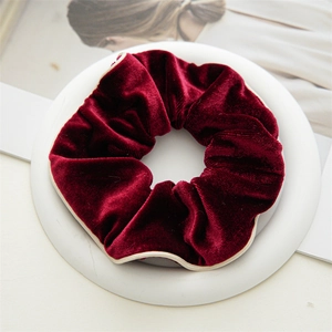 Detail of burgundy velvet scrunchie with contrast piping on a minimalist white tray
