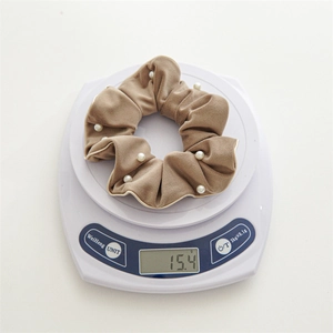 Detail shot showing a weight of 15.4g for this khaki velvet pearl scrunchie on a scale
