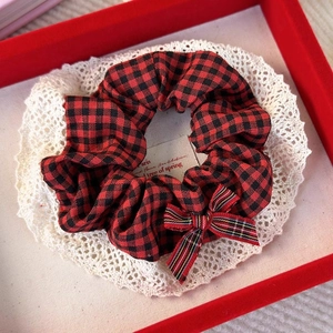Detail of red and black plaid scrunchie with bow decoration on a lace coaster