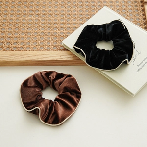Elegant velvet scrunchies in black and brown with white piping on a stylish background