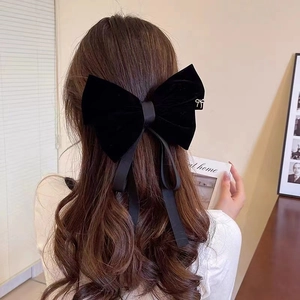 Detail of a large black velvet bow hair clip with a gold charm and long ribbon streamers