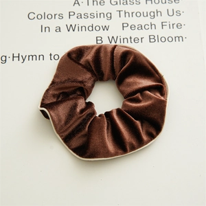 Close-up of brown velvet hair scrunchie with cream piping on minimalist backdrop