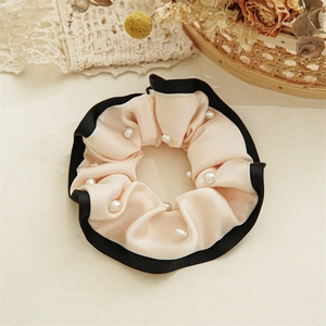Detail of pink satin hair scrunchie with black trim and elegant pearl embellishments