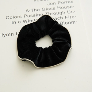 Detailed view of black velvet scrunchie with white piping on a vintage book page