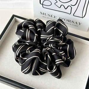 Macro detail of elegant black and white striped satin scrunchie with pleated silk texture