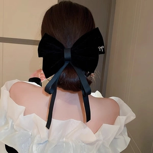 Detail of a large black velvet bow hair clip with long ribbons on a ponytail