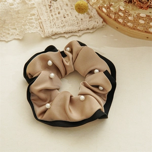 Detail view of premium champagne satin scrunchie with faux pearls and black edge trim