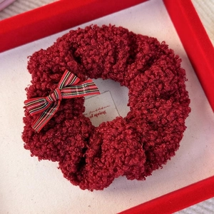Detailed macro of red plush lamb wool scrunchie with striped bow on display tray