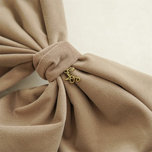 Macro detail of khaki velvet hair bow featuring a stylish golden cursive metal letter