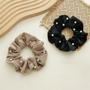 Detail view of velvet hair scrunchies with white faux pearls on wooden tray background